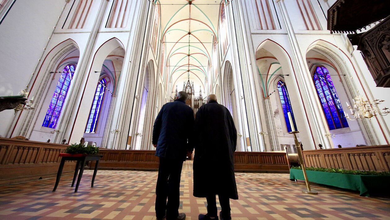 Günther Uecker bei der Einweihung der von ihm gestalteten Fenster im Schweriner Dom ©Wiebke Marchinkowski Zwei ältere Herren stehen in einer Kirche mit blauen Fenstern