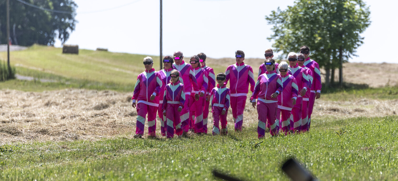 Landschaftstheaterprojekt „Überall ist Schöna – Eine Utopie im Jahre 2125“ Menschen in pinkfarbenen Anzügen spazieren in der Landschaft